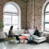 Twee digital marketing experten met laptop op de schoot die in een verlichte hoek van het kantoor overleggen waarbij 1 in de zetel zit en de andere in een stoel