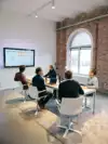Overleg tussen 5 digital marketing experts die aan een tafel kijken naar een TV scherm op de muur