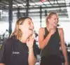 Twee jonge vrouwen in zwart trainingsshirt die lachend naar iemand kijken